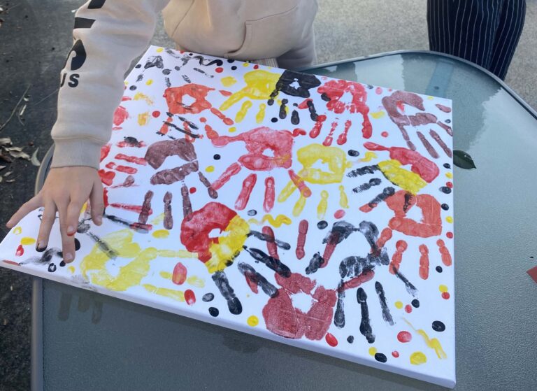 A canvas is being covered with red, black and yellow hand prints to celebrate ATSI Children's Day